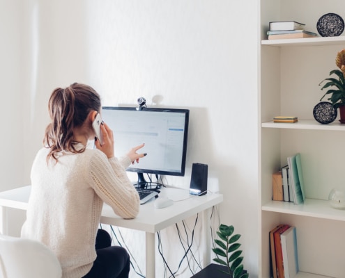 Shows a woman on the phone and looking at the computer. Represents seo services for therapists at Simplified will help support you with your counseling website