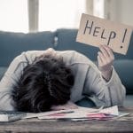 A woman sits with her head on a desk holding a sign that reads, "help!' She is regretting not setting up SEO services with Simplified SEO Consulting.