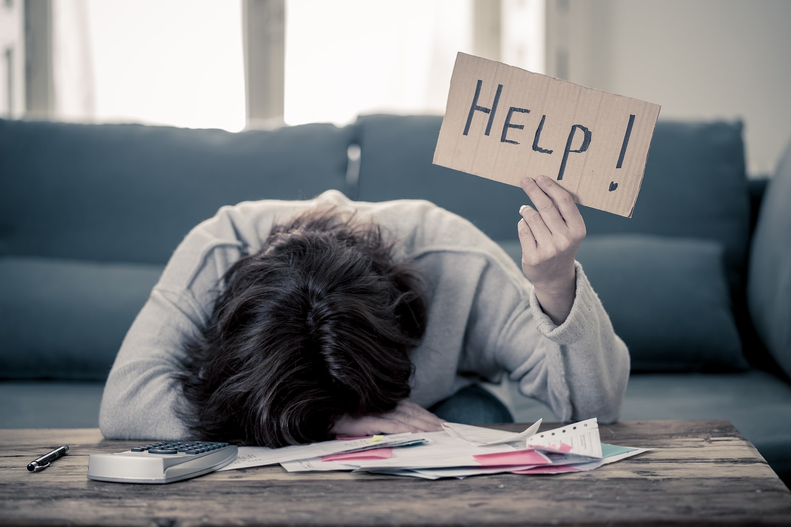 A woman sits with her head on a desk holding a sign that reads, "help!' She is regretting not setting up SEO services with Simplified SEO Consulting.