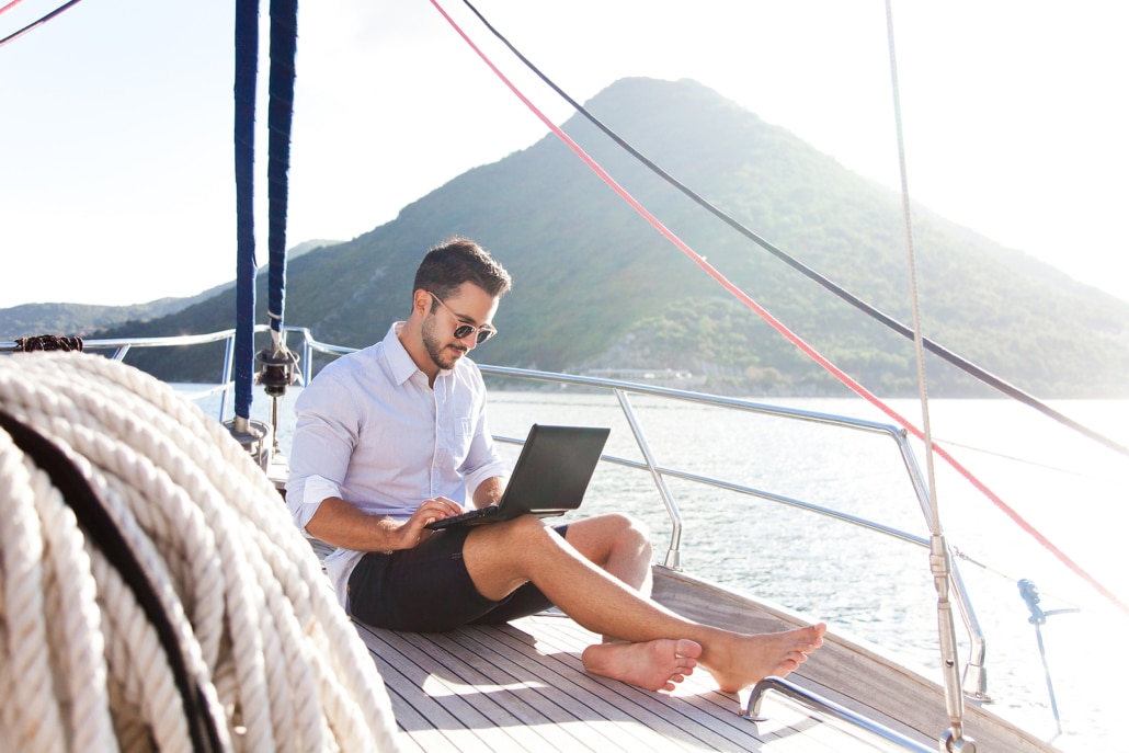 A man working on a laptop while in the middle of the ocean on a boat. Representing how you can do our DIY online SEO courses from anywhere! Schedule a free consultation with us today.