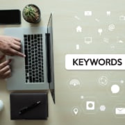 Photo of a person's hands using their computer next to a graphic of the word keywords in a search bar. This photo represents the way counselors can use mental health keywords and counseling keywords to improve their SEO through blogging.