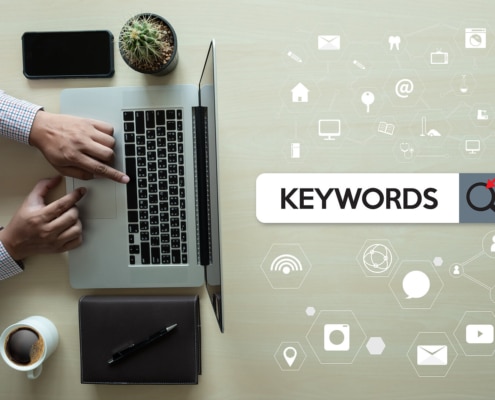 Photo of a person's hands using their computer next to a graphic of the word keywords in a search bar. This photo represents the way counselors can use mental health keywords and counseling keywords to improve their SEO through blogging.