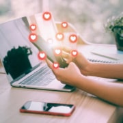 A close up of someone holding a phone with heart icons around it. Represents how blogging is a great way to boost SEO rankings for private practice SEO.