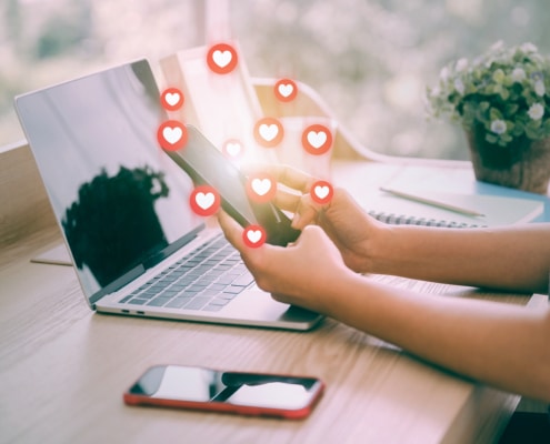 A close up of someone holding a phone with heart icons around it. Represents how blogging is a great way to boost SEO rankings for private practice SEO.
