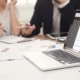 Photo of a laptop with data pulled up and two employees talking in the background. Represents how private practice seo benefits therapists who are too busy to learn themselves. They can have a team member learn and still benefit.