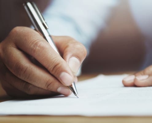 A picture of someone sitting at their desk and holding a pen in their right hand to write on a note book. This represents how you can write your blogs to boost your SEO with Simplified SEO Consulting