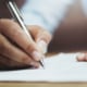 A picture of someone sitting at their desk and holding a pen in their right hand to write on a note book. This represents how you can write your blogs to boost your SEO with Simplified SEO Consulting