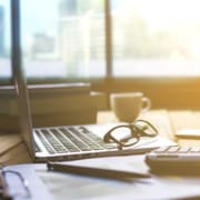 A laptop rests on a workstation with glasses and papers. Learn how technical SEO can offer support for improving counselor SEO by contacting an SEO specialist for therapists.
