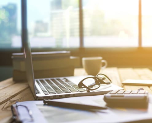 A laptop rests on a workstation with glasses and papers. Learn how technical SEO can offer support for improving counselor SEO by contacting an SEO specialist for therapists.