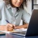 Woman looking at her computer and writing things down. Representing how SEO for therapists can help during Covid-19