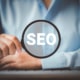 Woman holding a magnifying glass displaying the words SEO. Represents how personal injury lawyers can use SEO to reach their ideal clients. Start today.