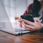 Photo of a woman using her laptop and cell phone with a search bar over the image. This photo represents the simple way of incorporating internal links into your service pages.