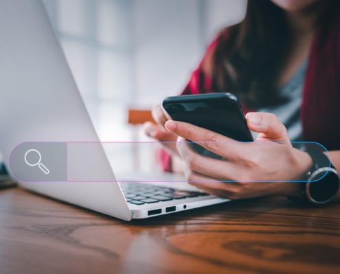 Photo of a woman using her laptop and cell phone with a search bar over the image. This photo represents the simple way of incorporating internal links into your service pages.