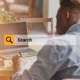 Image of a man at a laptop overlayed by an orange search bar. Which highlights the importance of knowing how to write a meta description for a private practice website. Especially for a therapists about page when it comes to their SEO.