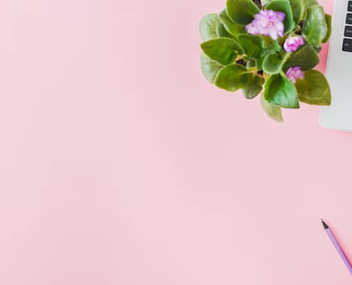 Pink table with a laptop, coffee and flowers on it representing the process of blogging to improve SEO.