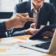 Two people work on laptop and tablet with papers on a table. Want to learn the best healthcare SEO strategy? Work with us today to make healthcare SEO work for you!