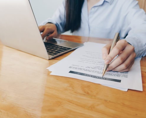 A woman writes on a paper while working on a laptop. Want to learn more about SEO in healthcare? Our services can help you incorporate healthcare SEO into your website.