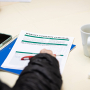 A person’s hand about to write on a piece of paper with a phone and cup next to them. Trying to find the best way learn about SEO practices? Our SEO services can you flourish.