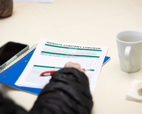 A person’s hand about to write on a piece of paper with a phone and cup next to them. Trying to find the best way learn about SEO practices? Our SEO services can you flourish.