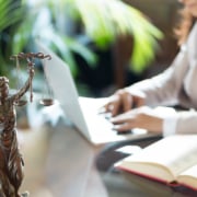 Lady Justice on a desk with individual typing on a laptop. We are here to help your law firm grow with SEO techniques. Learn more about SEO keywords and ads here.