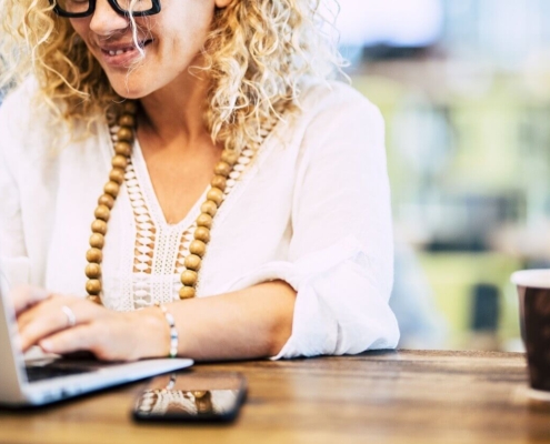 Smiling woman wearing white working on laptop. Learn to work on your private practice SEO with the help of Simplified SEO Consulting.