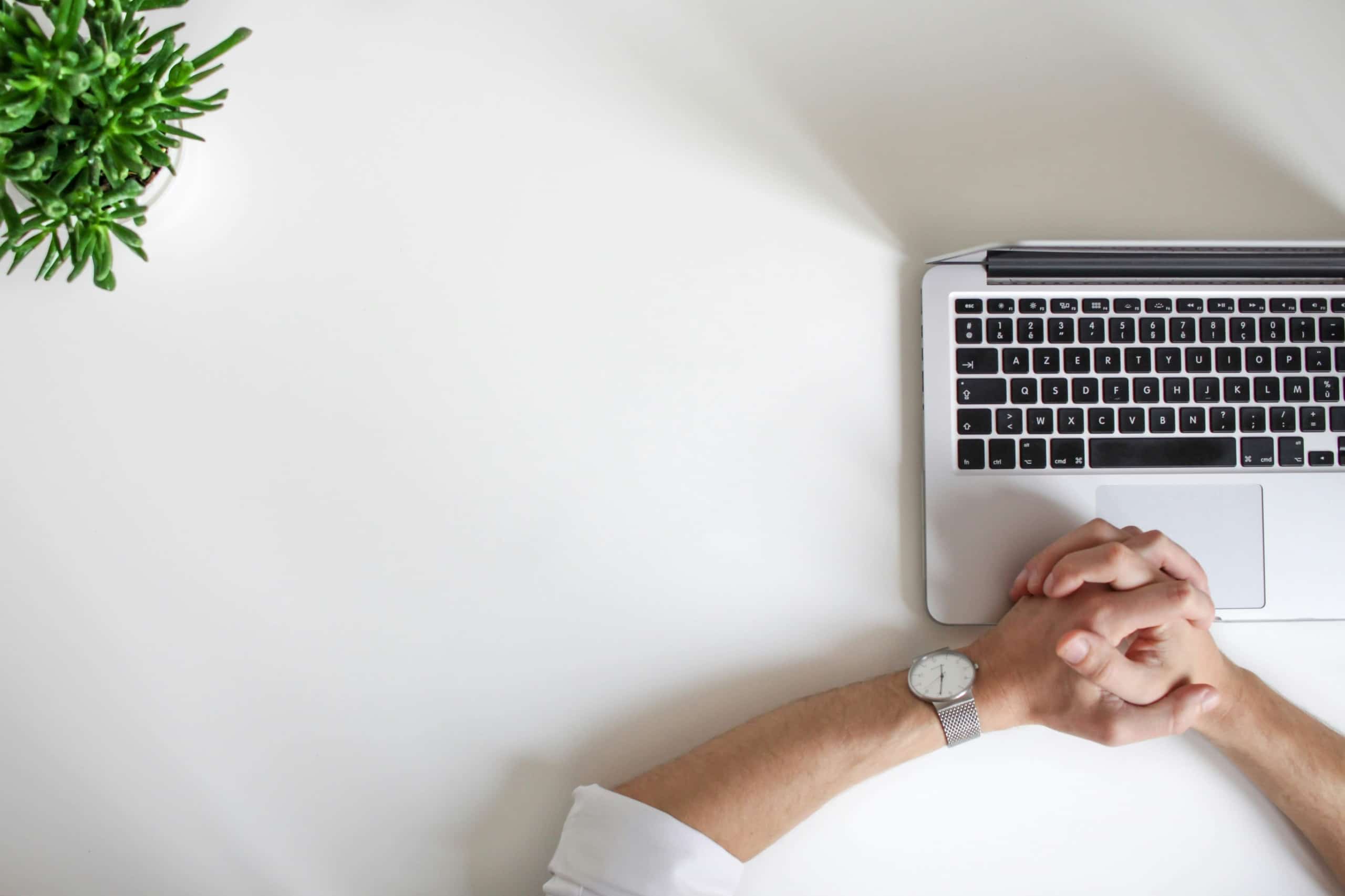 Image of a man's hands folded on a laptop. Learn how SEO for therapists can help your private practice's visability.