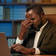 A business man sitting at a desk while pinching in between his eyebrows. This represents how there are common SEO mistakes when doing it yourself. Learn how to avoid these mistakes here!