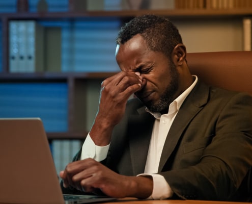 A business man sitting at a desk while pinching in between his eyebrows. This represents how there are common SEO mistakes when doing it yourself. Learn how to avoid these mistakes here!