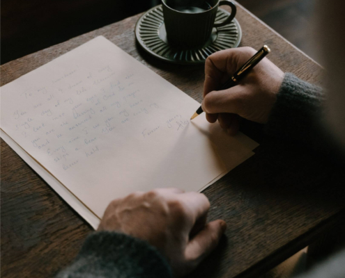 Shows a therapist writing a blog with a pencil on notebook paper at a desk with a coffee cup. Represents how seo for online therapy and how seo for online therapist can boost website visibility.