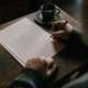 Shows a therapist writing a blog with a pencil on notebook paper at a desk with a coffee cup. Represents how seo for online therapy and how seo for online therapist can boost website visibility.