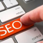 Finger pushing SEO orange laptop keyboard key. Discover how you can begin finding your ideal clients with the help of SEO.