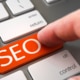 Finger pushing SEO orange laptop keyboard key. Discover how you can begin finding your ideal clients with the help of SEO.