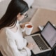 A woman in glasses and a cozy sweater works on her laptop while holding a cup of tea, symbolizing search engine optimization for counselors and SEO marketing for therapists.