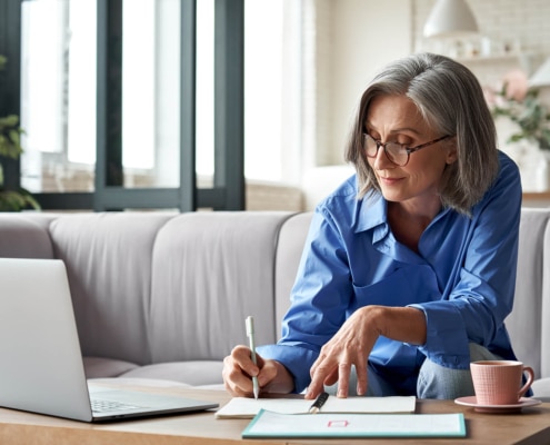 Image of a mature woman writing in a journal while in front of a laptop. Start finding your ideal clients with the support of Simplified SEO consulting.