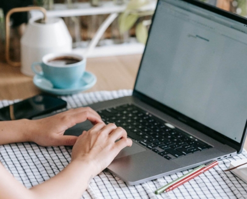 Person typing on a laptop with a coffee cup nearby, focusing on blog content using search engine optimization for counselors and counselor SEO techniques.