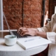 A person typing on a laptop at a café table, working on content strategy. This represents an SEO copywriting service and the importance of copywriting blogs for SEO to improve online visibility.
